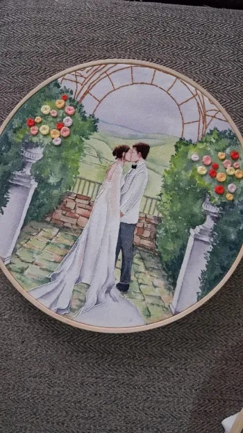 Bordado de um casal de noivos se beijando sob um arco de flores