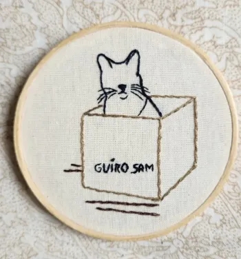 Bordado de um gato dentro de uma caixa com o nome Guiro Sam