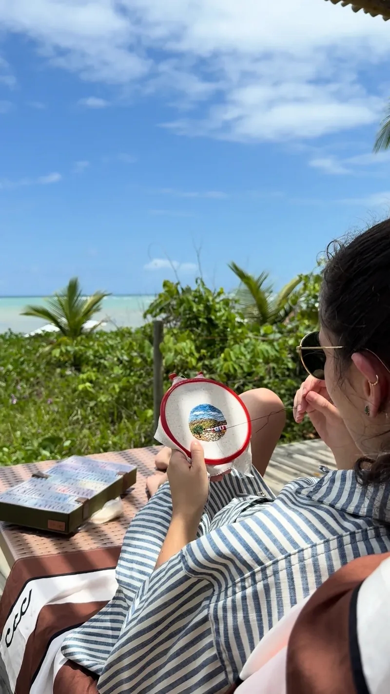 Bordadeira bordando uma paisagem de praia ao ar livre, de frente para o mar