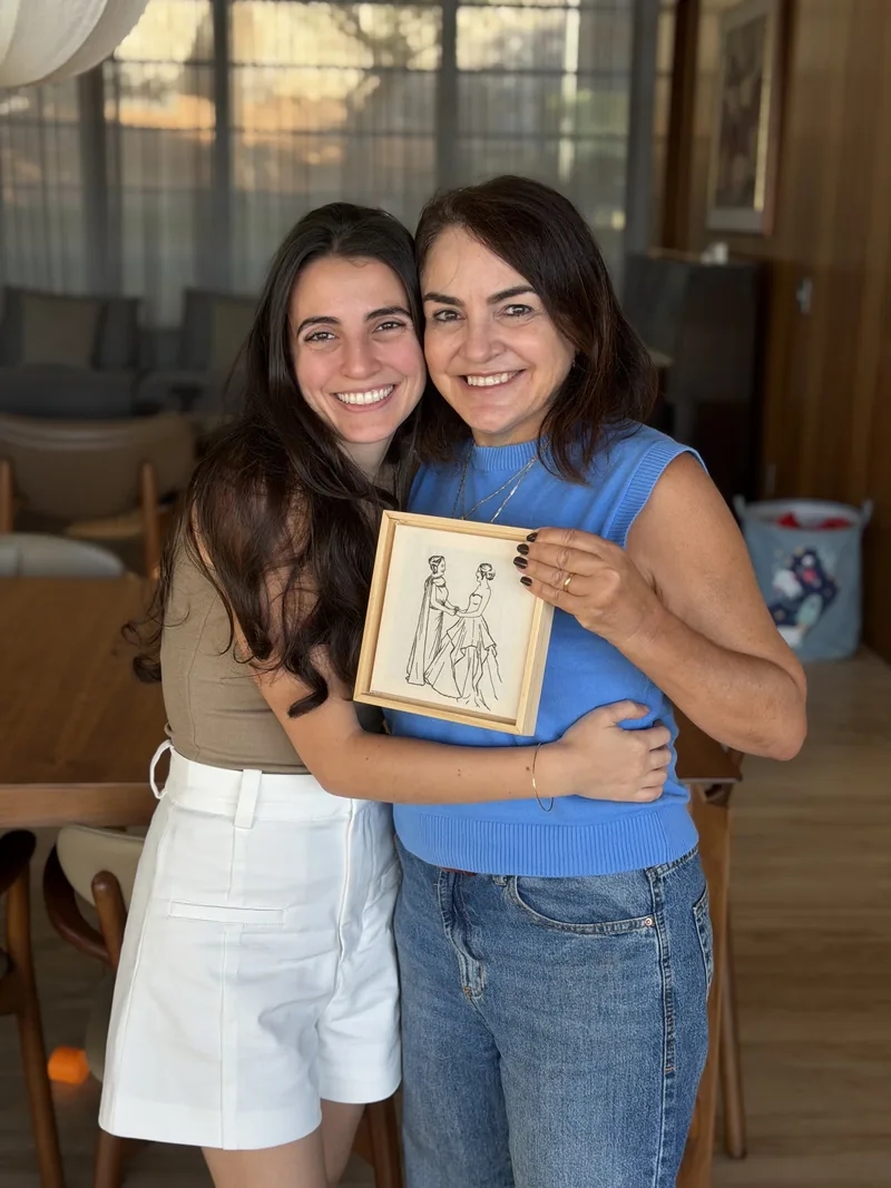 Mãe e filha abraçadas segurando um bordado emoldurado de presente